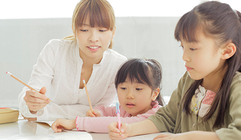 小さな女の子2人と女性が鉛筆をもって何かを書いている