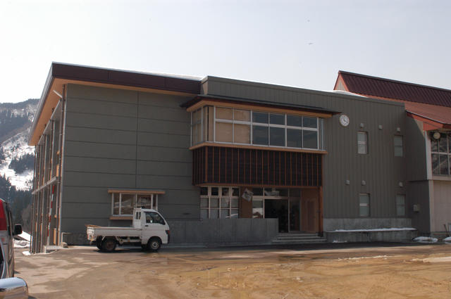 濃いグレー色の外壁で、右上に時計が設置された2階建ての旧東中江小学校の建物外観の写真