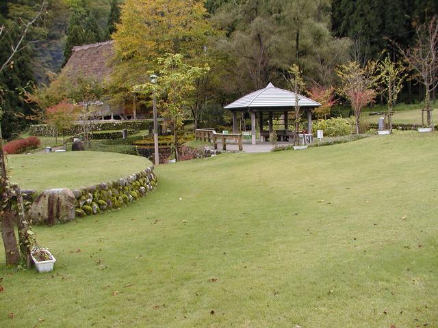 広々とした芝生の奥に東屋が見える民謡の里公園内の写真