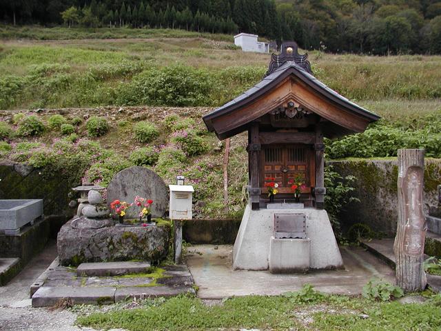 屋根の付いた祠のような構えで生花が活けてあるお小夜塚を正面から写した写真