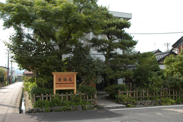 入口を大きな木や植物に囲まれた愛染苑の木で造られた看板などを全体的に撮影した写真
