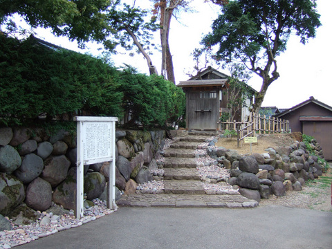 左側手前に白い案内板があるすぐ横に上へと上がる階段があり、階段の先に市指定文化財福光城址栖霞園がある写真