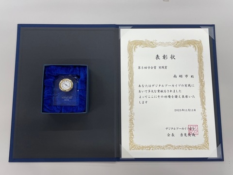 デジタルアーカイブ学会実践賞の賞状と、ケースに入った記念品の時計の写真