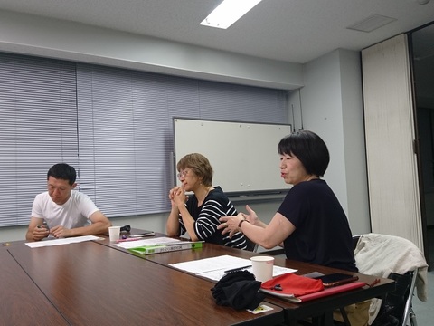 1名の男性、2名の女性が同じテーブルの席に座り、手前に座っている女性が身振り手振りを交えて話をしている様子の写真