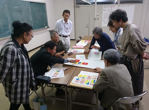 参加者が集まり、テーブルの上に置かれた紙を見ながら話し合いが行われている写真