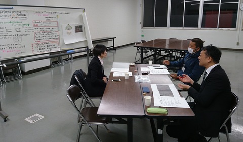 沢山の文字が書かれた紙がホワイトボードに貼られている前の席で、3人の参加者が話し合いを行っている写真