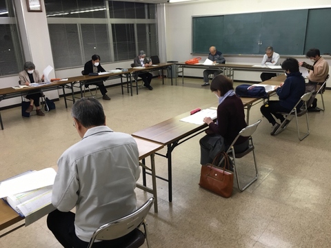 室内全体を使って長机がロの字型に設置された席に参加者達が間隔をあけて座り、会議が行われている写真