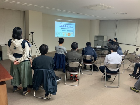 参加者達がパイプ椅子に座り壁に映し出された資料を見ている様子を後方から撮影した写真