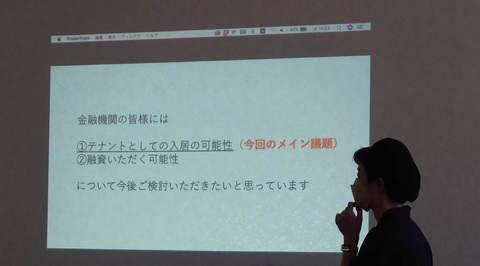「金融機関の皆様には」と書かれた資料が映し出された壁をアップで写した写真