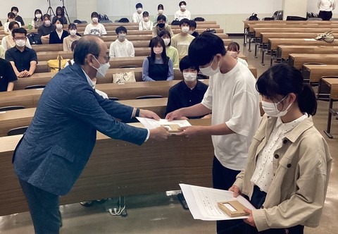 女子学生と男子学生が田中市長から任命状を交付されている写真