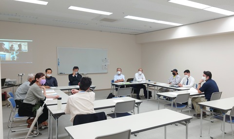 壁にパソコンの画面が映し出された室内で、参加者達が話し合いを行っている写真