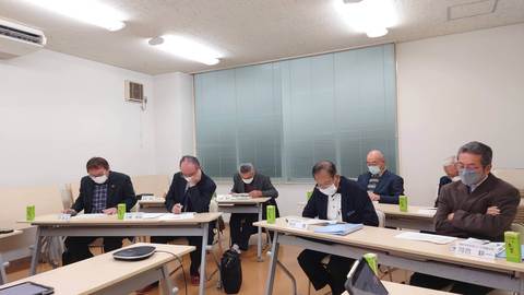 長机の席に着き、手元の資料に目を落としている男性参加者たちの写真