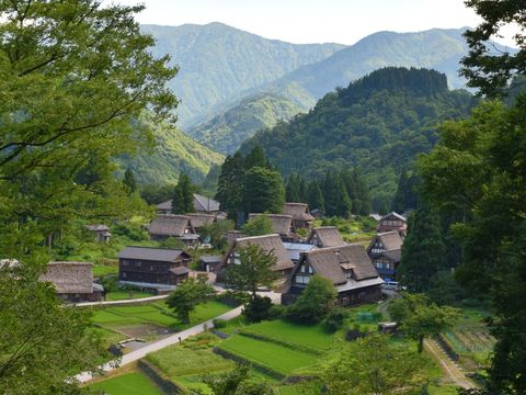 周りを山々に囲まれた中に相倉合掌造りの集落がある写真