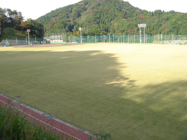 奥に緑の山がみえ、手前に広々とした芝生のグランドの写真
