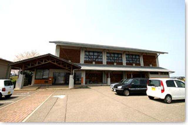 手前に駐車場、左側歩道の奥に入り口がありそのまま建物が連なっている高瀬ふれあい体育館を正面から写した写真