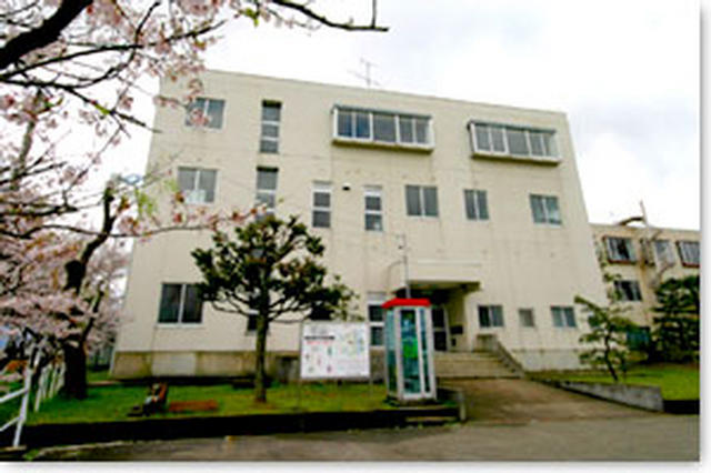 体育館敷地内に電話ボックスがありその奥に白い外壁の南砺市旅川体育館の全体を写した写真