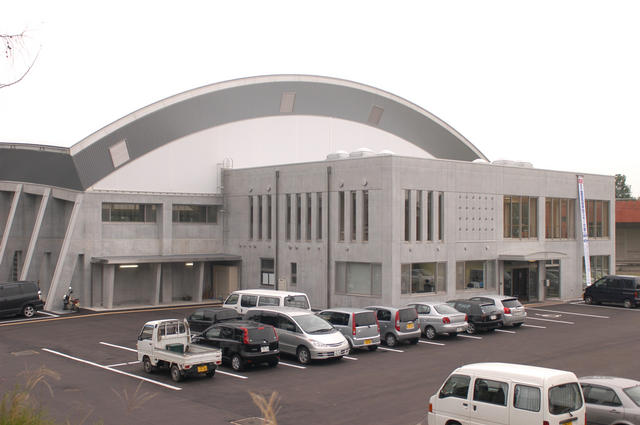 駐車場の奥にUFOを逆さまにした形状の屋根の建物に四角の箱の建物がくっついている城南屋内グラウンドの写真