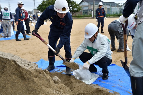2名1組でスコップを使い砂を袋にいれている写真