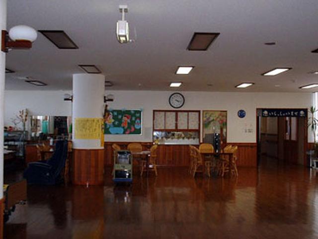 部屋の真ん中に大きな丸い柱があり、テーブルが並び壁には時計が飾られた機能訓練室の写真