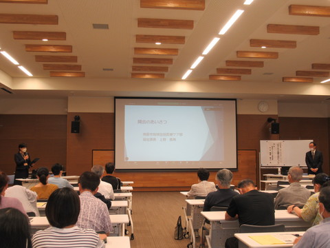 資料が映し出された大型スクリーンが設置された会場の前方右側に立っている男性を、左にマイクを持って進行している女性が紹介している様子を2人ずつ座っている参加者が聞いている、ひきこもりサポートセミナーの様子の写真
