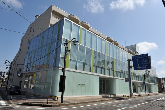 2階から全面ガラス張りの南砺市立中央図書館を道路越しに斜め前から撮影した写真