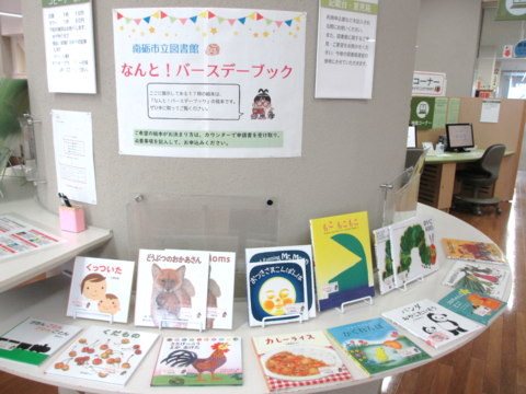 中央図書館内の円柱の壁に「なんと！バースデーブック」と書かれたポップの下のスペースにプレゼント絵本が飾られている写真