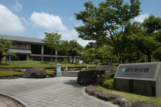自然に囲まれた福光美術館の入り口にある看板と舗装された建物までの道を撮影した写真