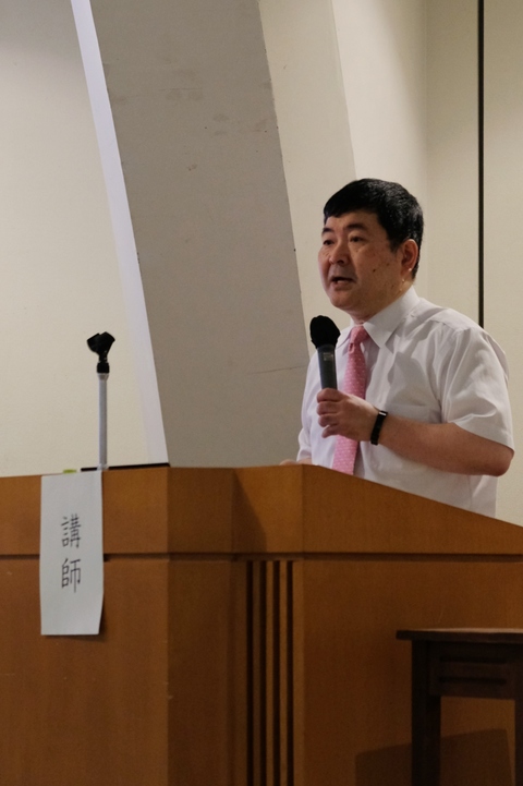 講師の明橋大二氏が演台でマイクを持ち話をしている写真