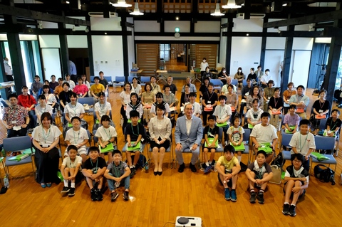 広い会場に置かれた椅子に座る参加者たちを写した集合写真