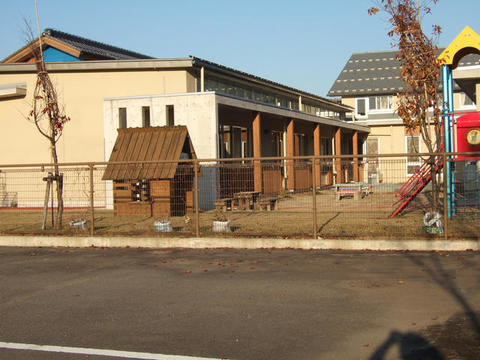 横長の園舎の前に園庭があり、滑り台などの遊具のある保育園の外観写真