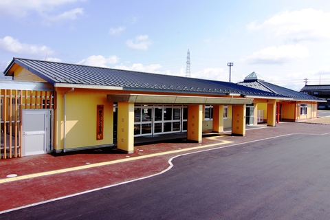 黄色い外壁で平屋建て、横長の園舎で「福光どんぐり保育園」と書かれた木製の看板が設置されている福光どんぐり保育園の外観写真