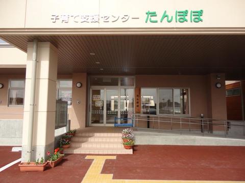 「子育て支援センター たんぽぽ」と掲示され、玄関前に数段の階段とスロープが設置されている建物の入り口を写した写真
