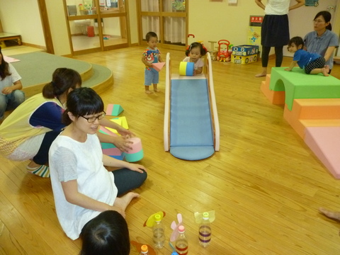 施設の中で、ペットボトルのおもちゃで遊ぶ親子や滑り台からおもちゃを転がそうとして遊んでいる幼い子どもを写した写真