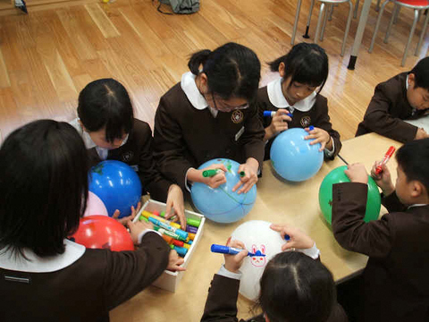青や緑、白の風船にマジックで絵をかいている子供たちの写真