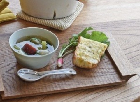 木製のトレイの上にボールに入ったスープ、パン、ラディッシュのような野菜が置かれている写真